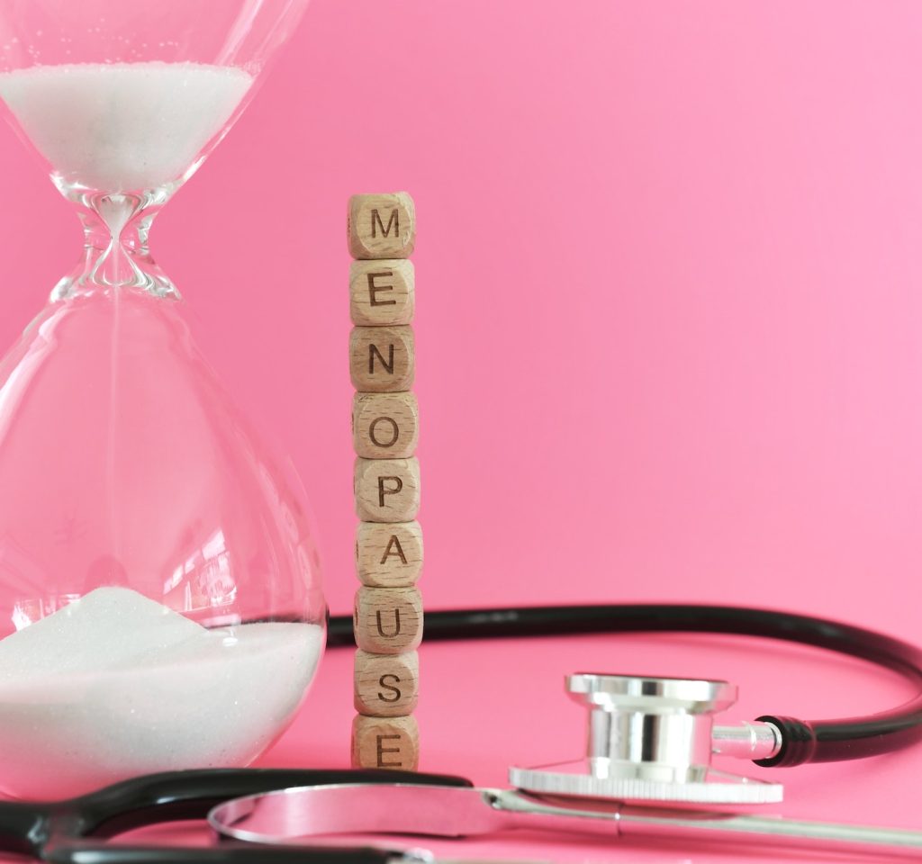 Menopause with stethoscope and hourglass on pink background. Going through the change.